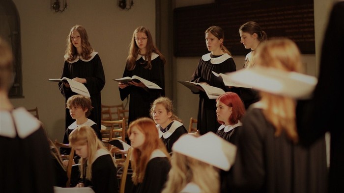 Ein Chor junger Sänger in festlichen Roben tritt in einer traditionellen Kirche auf.