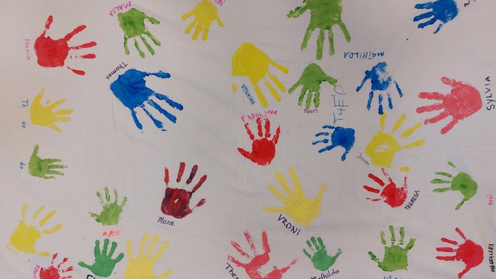 Bunte Handabdrücke auf weißem Papier, jedes mit Namen beschriftet