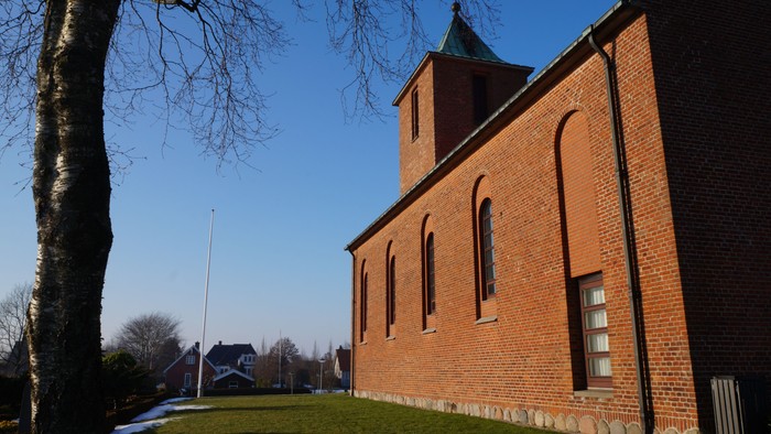 En rød murstenskirke med tårn og et flagstang.