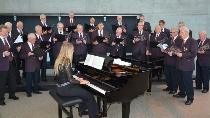 En kvinde spiller piano mens en mandskor synger.