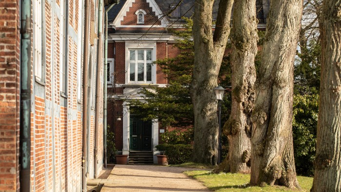 Ein rotes Backsteingebäude mit weißem Türrahmen und einem Weg, der zu einem Haus führt, umgeben von Bäumen