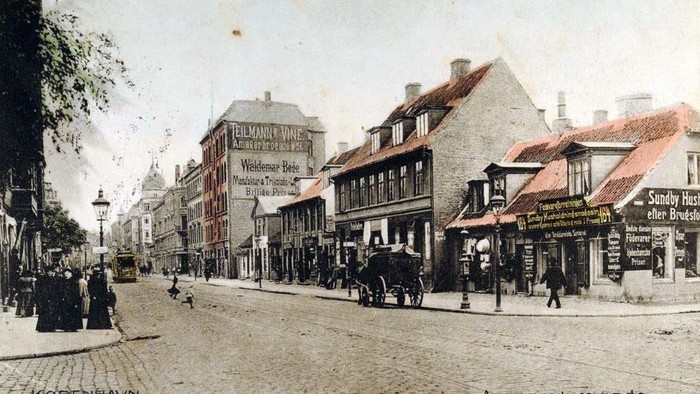 Gammelt gadebillede af Amagerbrogade i København med hestetrukne vogne og bygninger fra begyndelsen af 1900-tallet.