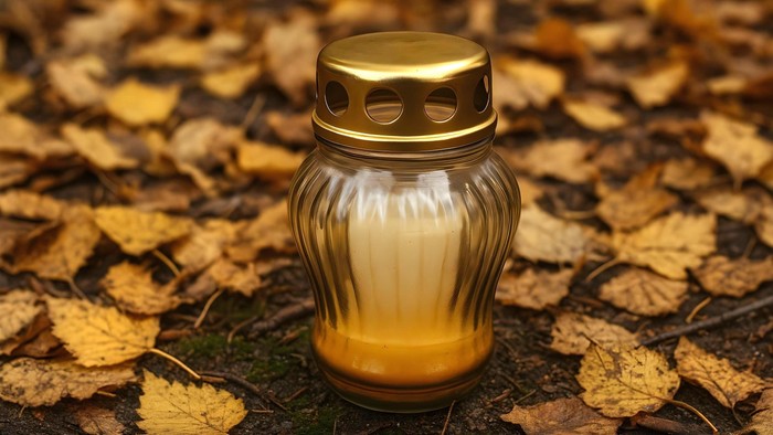 Goldener Votivkerzenhalter, umgeben von Herbstblättern auf dem Waldboden.