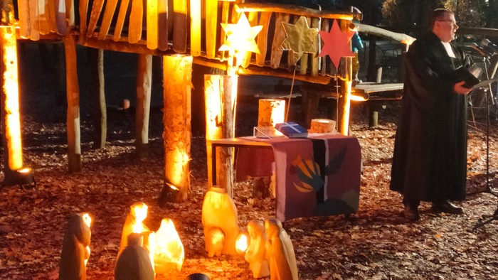Ein Mann in einem Gewand steht in der Nähe einer Weihnachtskrippe mit brennenden Kerzen.
