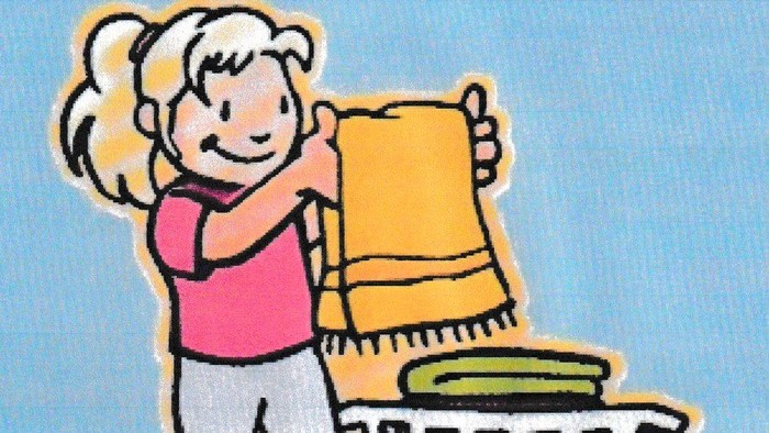 Ein Mädchen hält ein gelbes Handtuch und steht neben einem Wäschekorb.