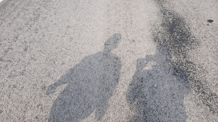 Schatten zweier Personen, die auf einer kiesigen Straße gehen.