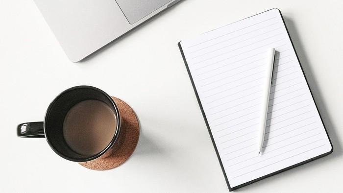 Bureau med laptop, notatbog, pen, mobiltelefon, kaffe og planter