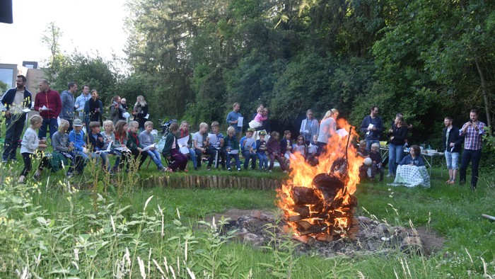En gruppe af mennesker står om en bålstapel i en eng.