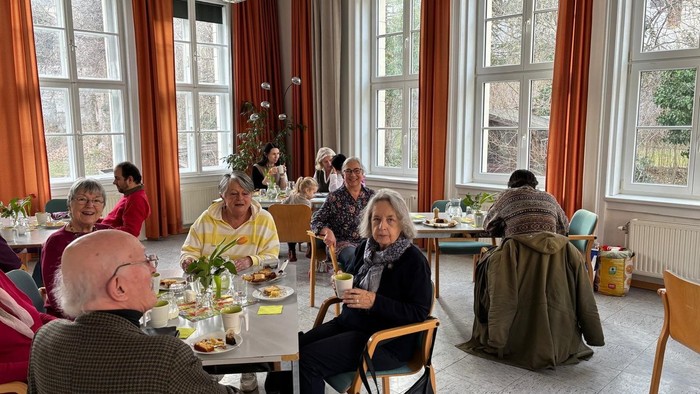 Gruppe von Menschen, die gemeinsam eine Mahlzeit in einem hellen, geräumigen Esszimmer mit großen Fenstern genießen.