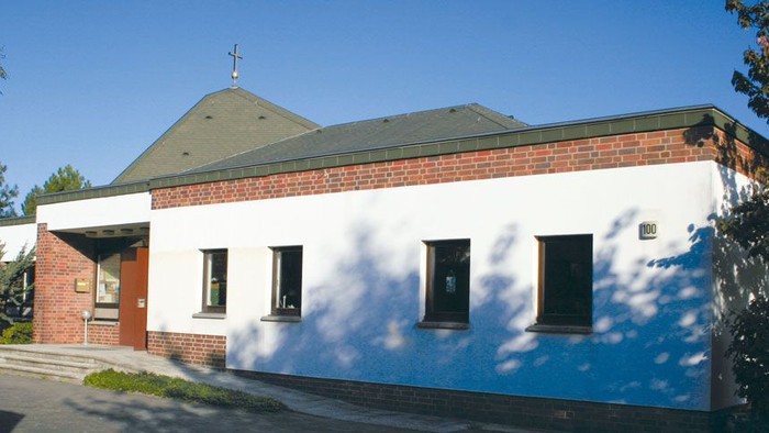 Modernes eingeschossiges Gebäude mit weißen Wänden, roten Backsteinakzenten und einem grünen Dach unter klarem blauem Himmel.