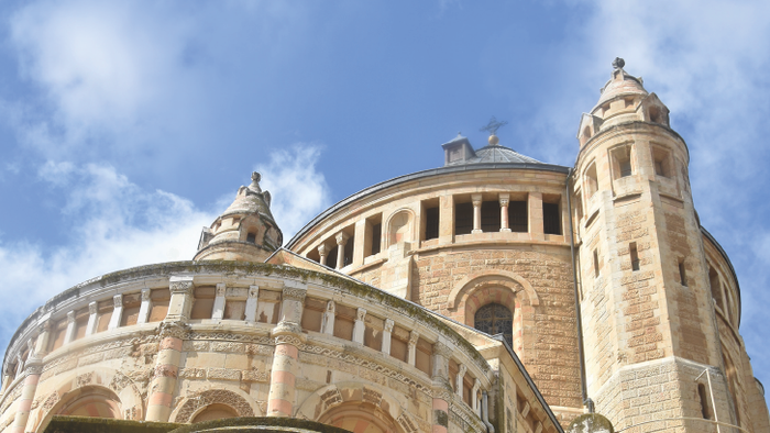 Historische Steinkirche mit runder Kuppel und Glockenturm unter einem strahlend blauen Himmel.
