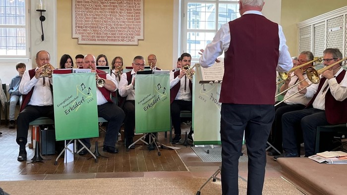 Eine Gruppe von Musikern, die in einer Kirche Blechblasinstrumente spielen, geleitet von einem Dirigenten.