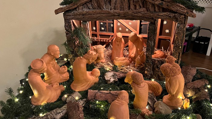 Handgefertigte Weihnachtskrippe mit Holzstall, Figuren und funkelnden Lichtern unter Grünpflanzen.