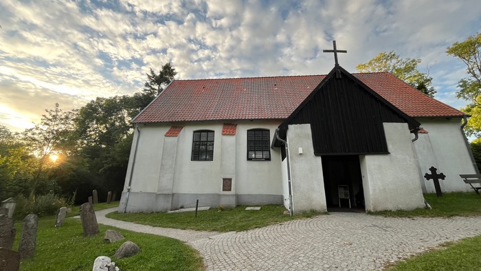 Idyllische alte Kirche mit Kopfsteinpflasterweg und Grabsteinen auf einem ruhigen, sonnenbeschienenen Friedhof.