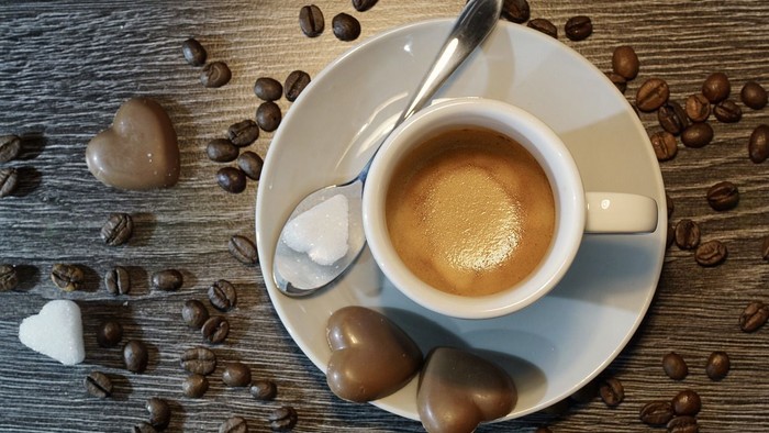 Eine Tasse Kaffee auf einem Holztablett mit Kaffeebohnen und Schokoladenherzen