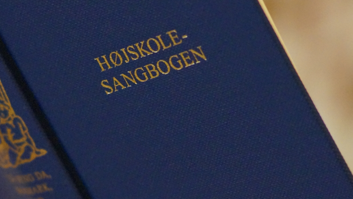 En hånd holder en blå bog med guldskrift.
