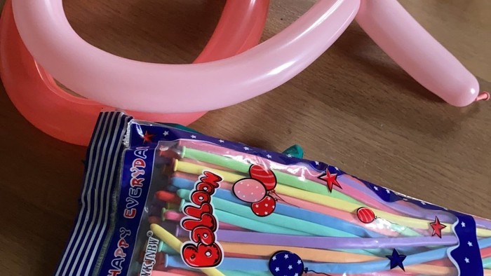 Ein rosa Luftballon liegt neben einem bunten Geschenk auf einem Tisch.