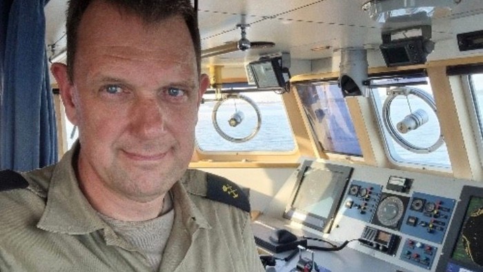 Foto af Peter Freisleben i uniform med et skibs navigationssystemer på broen og udsigt til havet i baggrunden