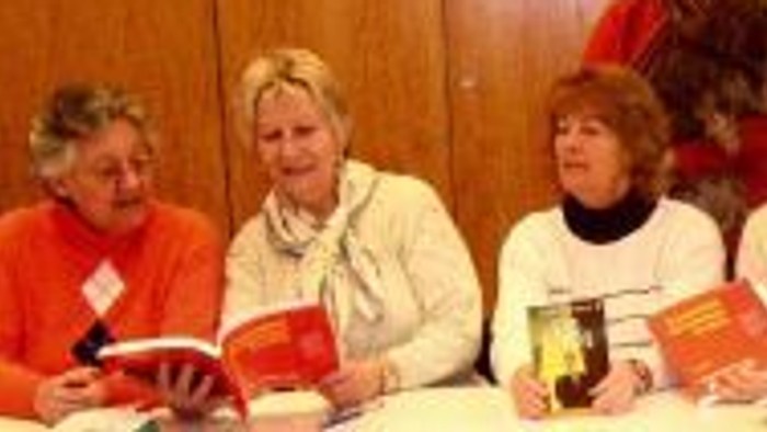 Drei Frauen an einem Tisch, die bei einer Buchveranstaltung oder Zusammenkunft Bücher signieren.