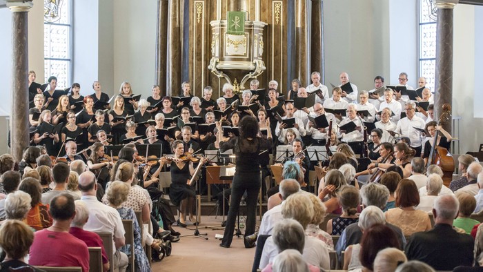 Ein großer Chor und ein Orchester treten in einer prächtigen Kirchenhalle vor einem aufmerksamen Publikum auf.