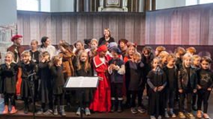 Ein Kinderchor tritt in einer Kirche auf, wobei ein Dirigent von vorne leitet.