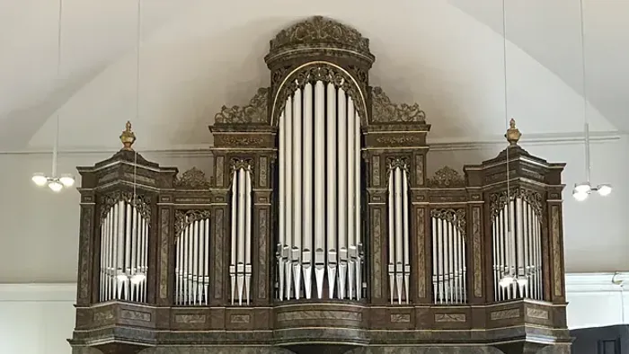 Elegante historische Pfeifenorgel mit aufwendiger Holzschnitzerei und verzierten Details in einer prächtigen Kirchenkulisse.