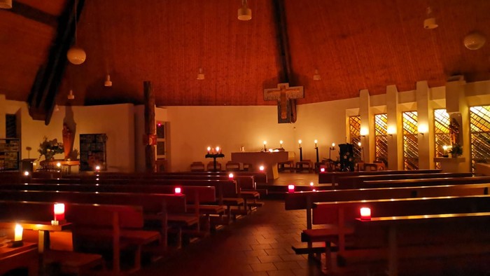 Kircheneingang mit Holzbänken und Kerzenlicht