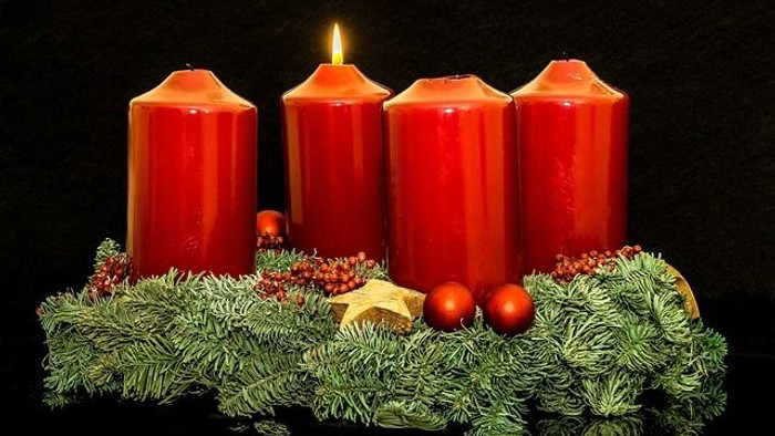 Vier rote Adventskerzen auf Grün mit Weihnachtskugeln