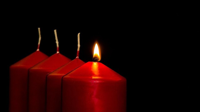 Drei rote Kerzen, eine angezündet, vor schwarzem Hintergrund