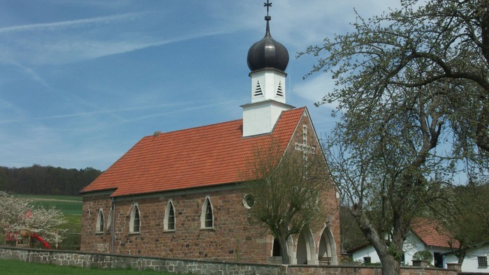 Idyllische Steinkirche mit rotem Ziegeldach und Glockenturm in einer malerischen Landschaft auf dem Land.