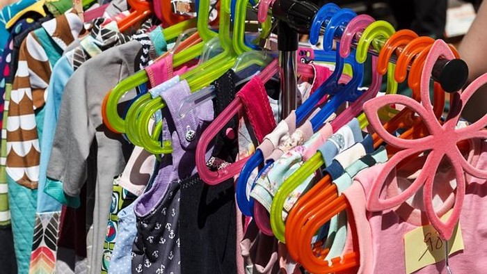 Bunte Kleiderbügel mit verschiedenen Kleidungsstücken auf einem Freiluftmarkt ausgestellt.