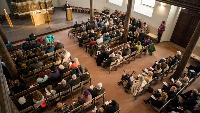 Eine überfüllte Gottesdienst mit Teilnehmern, die in Reihen sitzen und aufmerksam dem Redner vorne zuhören.