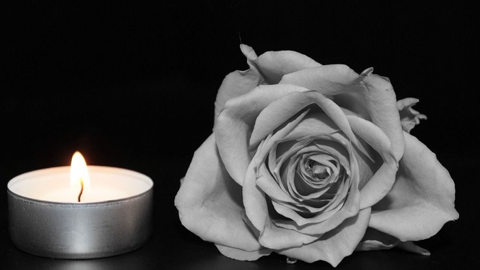 Eine brennende Kerze neben einer einzelnen Rose auf schwarzem Hintergrund