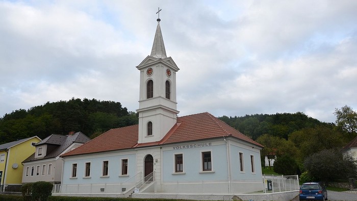 Kleine Kirche mit Uhrturm und rotem Dach in ländlicher Umgebung