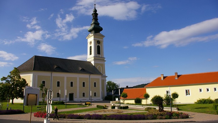 Weiße Kirche mit hohem Turm und rotem Dach auf gepflegtem Platz