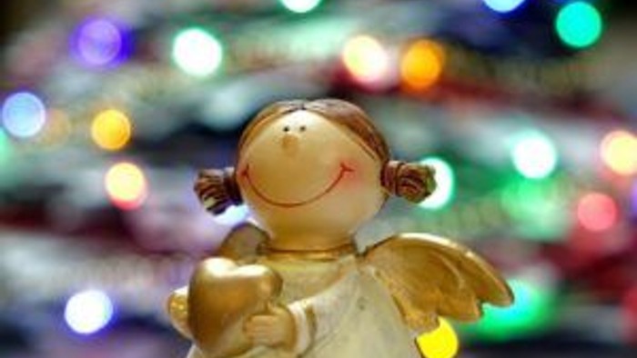 En lille engel-figur med gyldne vinger står foran en lyssjældet julested.