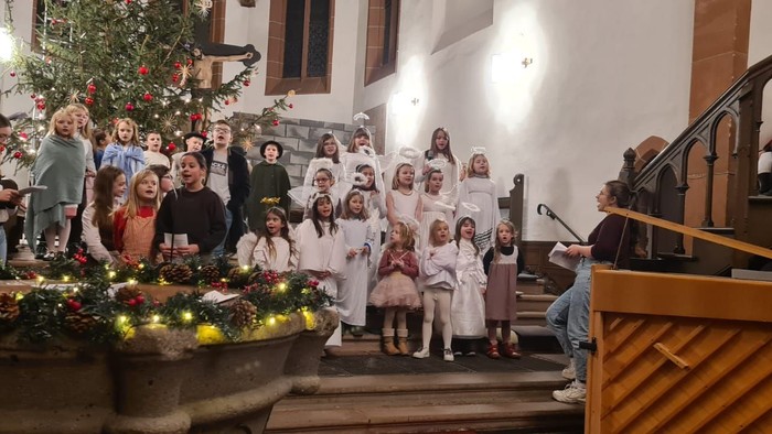 Ein festliches Weihnachtsfest mit Kindern in weißen Gewändern, die in der Nähe eines geschmückten Kircheneingangs und eines dekorierten Baumes singen.