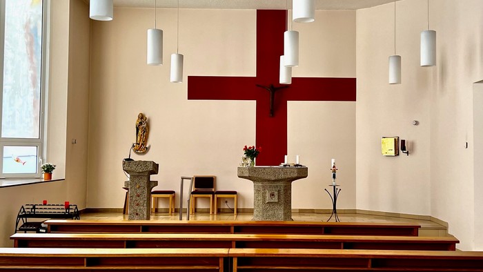 Die Kirche mit Holzbänken und einem großen roten Kreuz.