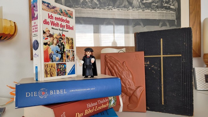 Eine Sammlung religiöser Bücher, ein Bibelatlas und eine kleine Figur auf einem Regal mit einem Druck des Letzten Abendmahls.
