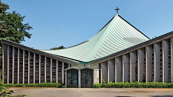Moderne Kirche mit schlankem, geschwungenem Dach und senkrechten Betonwänden, gelegen in einer gestalteten Grünanlage.