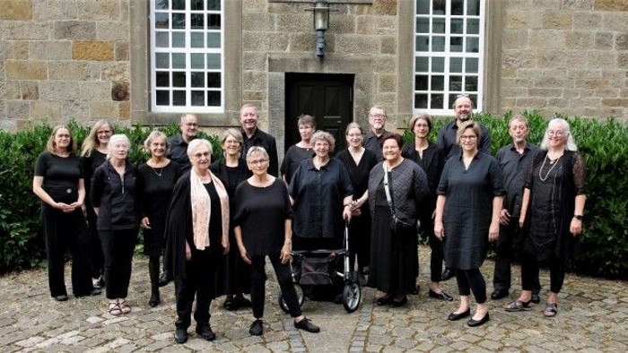 Eine Gruppe von Menschen in formeller schwarzer Kleidung posiert gemeinsam vor einem alten Steingebäude.