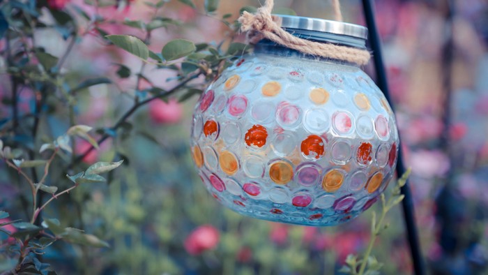 Bunte, gepunktete Glaslaterne, die zwischen blühenden Blumen und Grünpflanzen hängt.