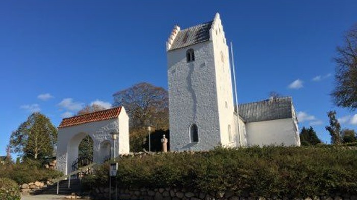 Et hvidt historisk tårn og kirke på en bakke med blå himmel.