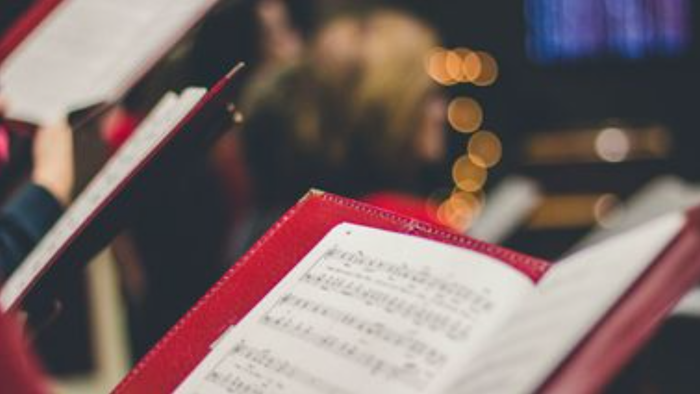 Ein Chor singt aus Notenbüchern, die auf einem Pult liegen.