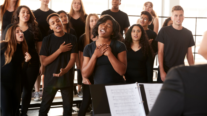 Eine vielfältige Gruppe junger Sänger tritt begeistert in einem Chor unter der Leitung eines Dirigenten auf.