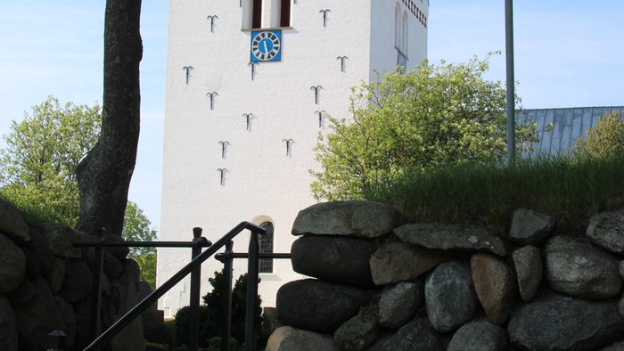 Historisk tårn med stentrin og mur, omgivet af grønt og en lygtepæl.
