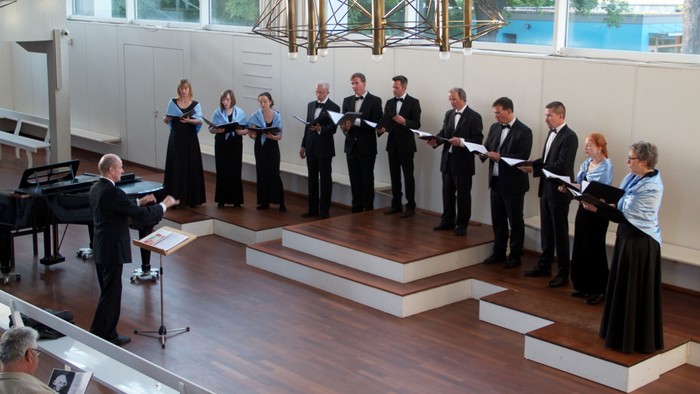Ein Chor proben in einem Raum mit Klavier und großen Fenstern.