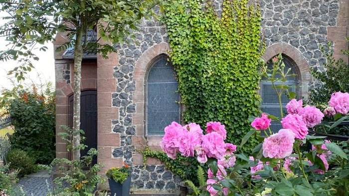 Steingebäude mit Rundbogenfenstern und pinkfarbenen Blumen davor.