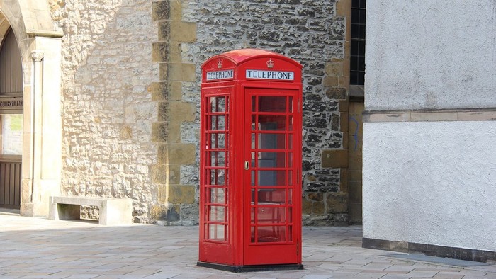 Klassische rote Telefonzelle steht vor einem alten Steingebäude mit bogenförmigem Eingang.