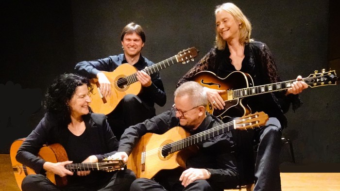 Eine Gruppe von vier Musikern, die in einer entspannten, intimen Atmosphäre verschiedene Gitarren spielen.